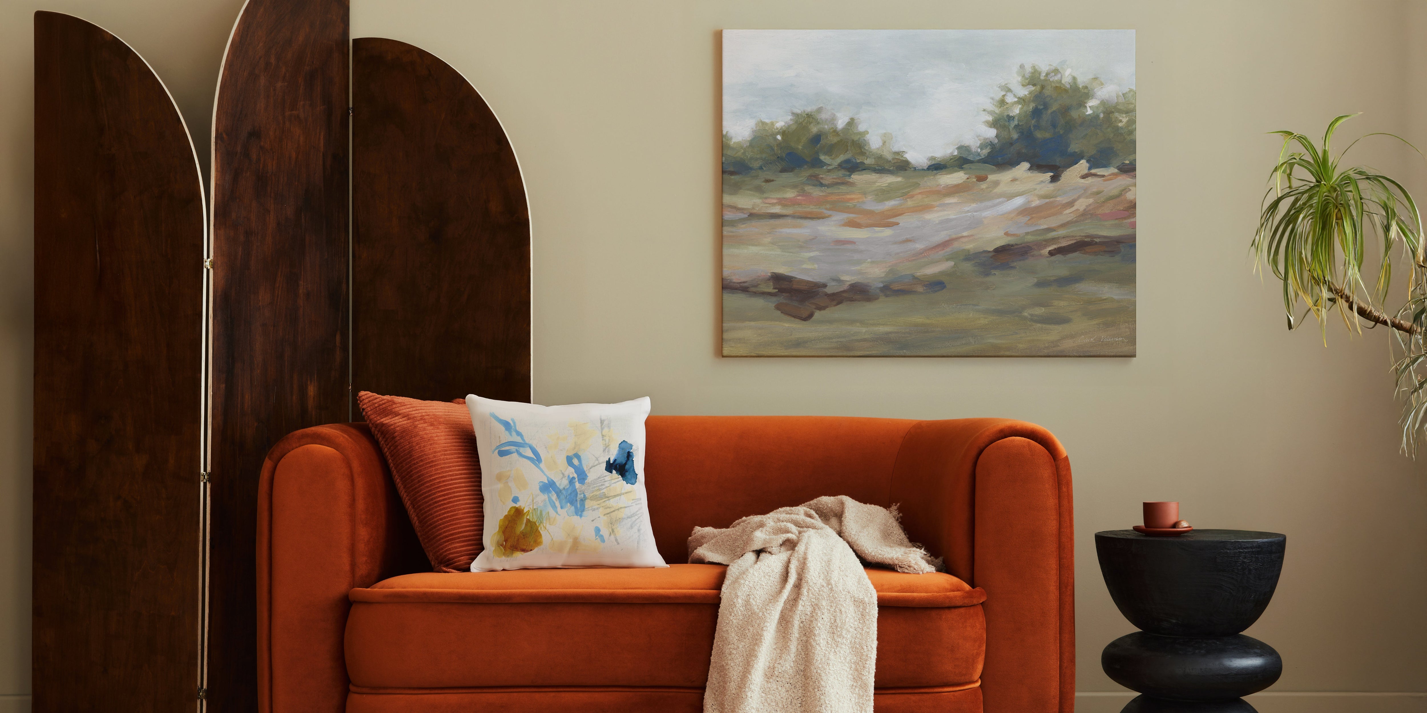 Orange sofa with decorative pillows and a plant in a room with a painting on the wall.